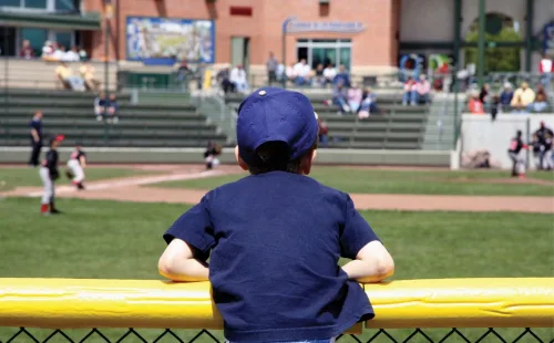 Little league player leaning on yellow SafeFoam foam padding along an outfield fence top