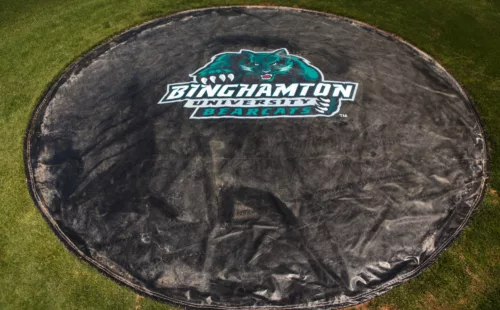 Custom black rain spot cover with printed graphics on a Binghamton University baseball field pitching mound