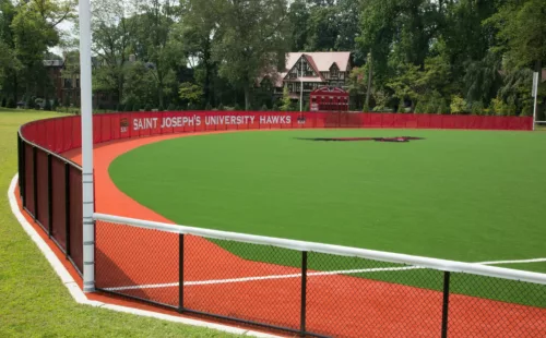 Red mesh baseball outfield fence windscreen on synthetic turf field at Saint Joseph's University Hawks