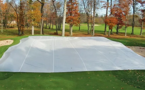 FieldSaver golf course green cover from CoverSports protecting a putting green in late fall, with fall foliage and fairway visible in the background