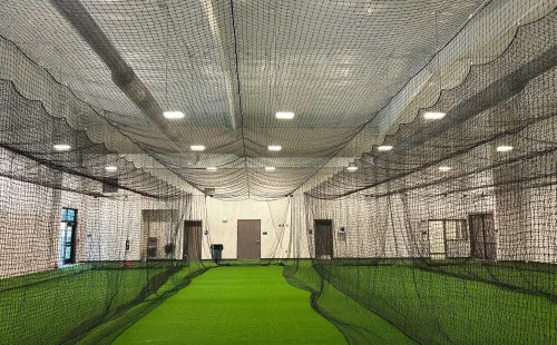 Multi-lane indoor batting cage system with black netting suspended over green turf hitting lanes in a training facility.