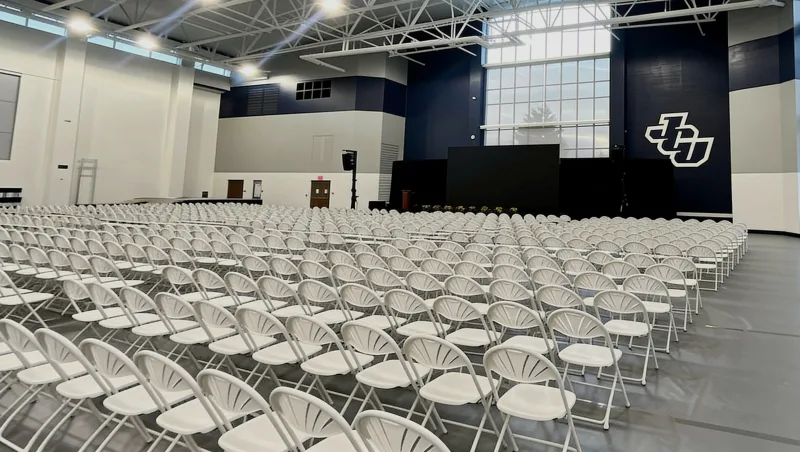 GymGuard gym floor cover protecting a hardwood gymnasium floor during a graduation ceremony setup with rows of folding chairs and a stage